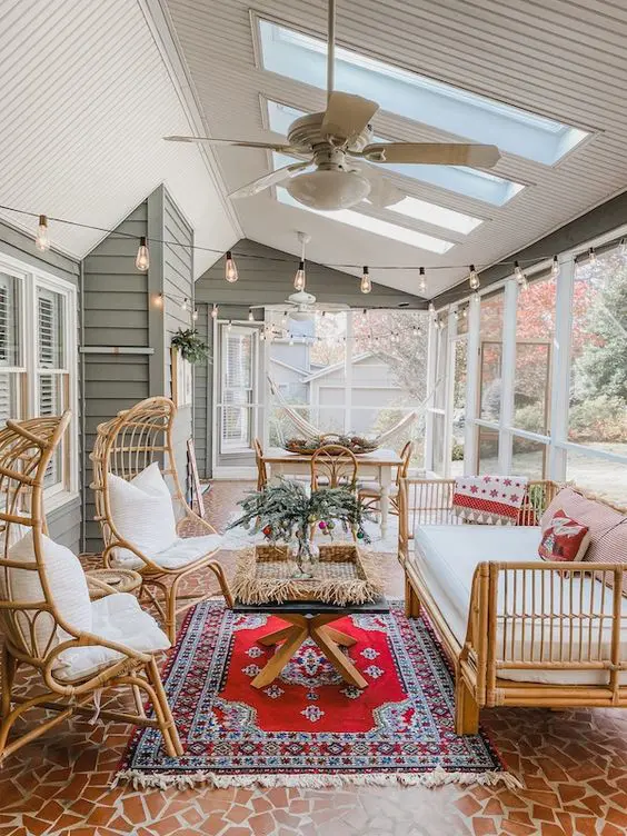 a boho screened porch with rattan furniture, a boho rug, a coffee table and a dining set with string lights over the space