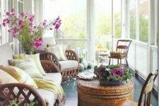 a bold screened porch with rattan furniture, a woven chest coffee table, potted plants and blooms and fall decor with pumpkins