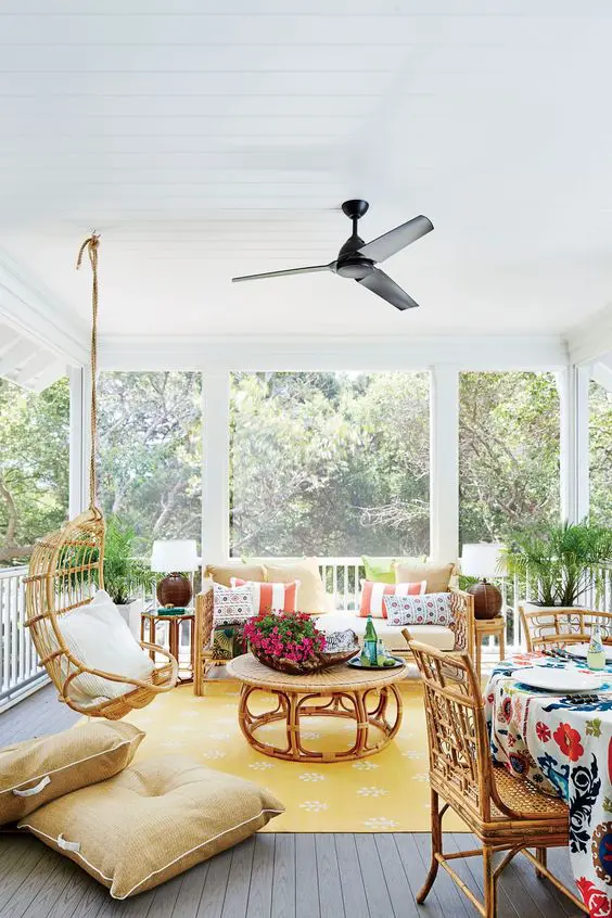 a bright screened patio with rattan furniture, bold and bright pillows and a rug, potted blooms and cool views