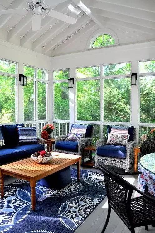 a bright screened patio with wicker seating furniture with navy upholstery, a low coffee table and some blooms and lanterns