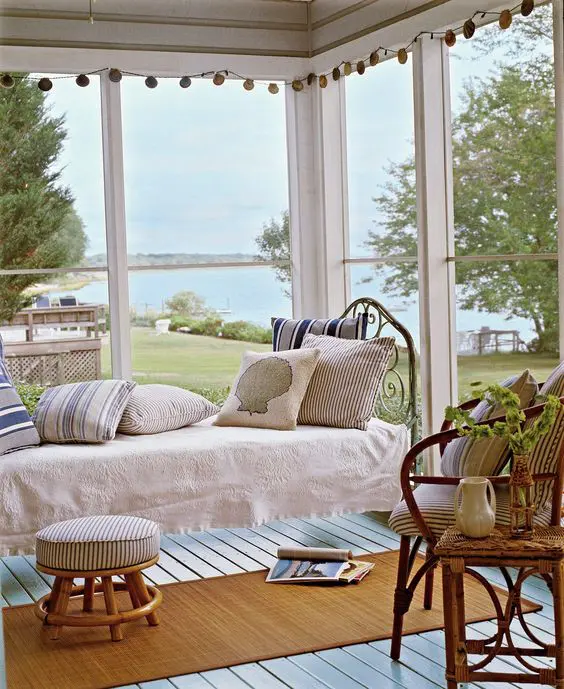 a coastal screened porch with a forged bed with pillows, a rattan chair and stools and potted greenery plus a sea view is wow