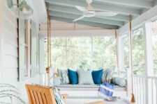 a coastal screened porch with a suspended daybed with pillows, a lounger, a blue ceiling and a blue rug