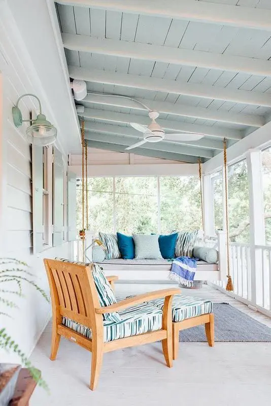 a coastal screened porch with a suspended daybed with pillows, a lounger, a blue ceiling and a blue rug