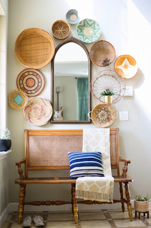 a colorful gallery wall of woven baskets, an arched mirror and a basket with a planter is a cool solution