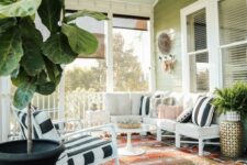 a colorful screened porch in boho style with a white corner sofa with printed pillows, rocker chairs, a boho rug, a round coffee table and greenery