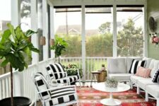 a colorful screened porch with white and black and white furniture, a colorful boho rug, potted plants and lanterns on the walls