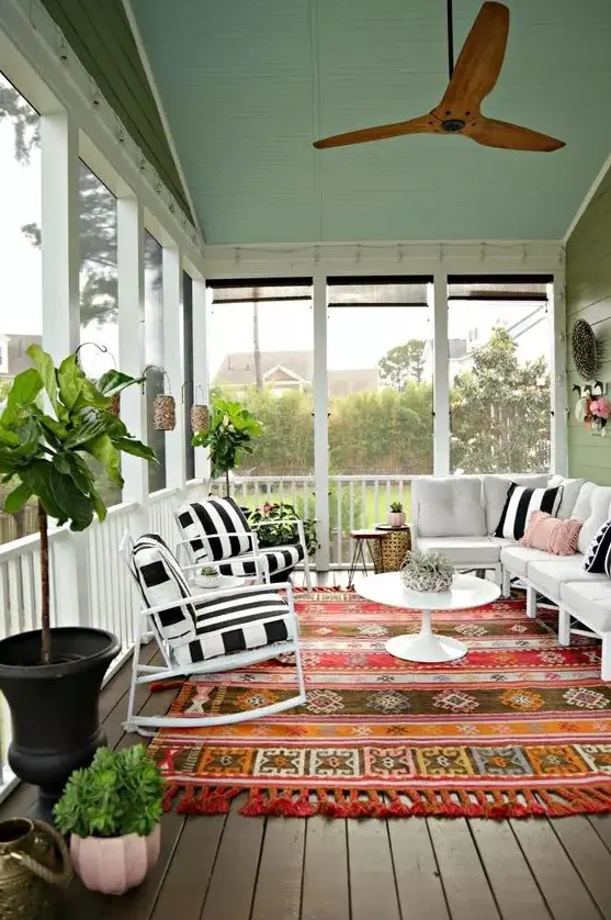 a colorful screened porch with white and black and white furniture, a colorful boho rug, potted plants and lanterns on the walls