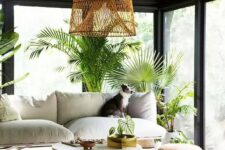 a contemporary boho screened porch with a white sofa, a round coffee table, a jute pouf, potted greenery and a woven pendant lamp