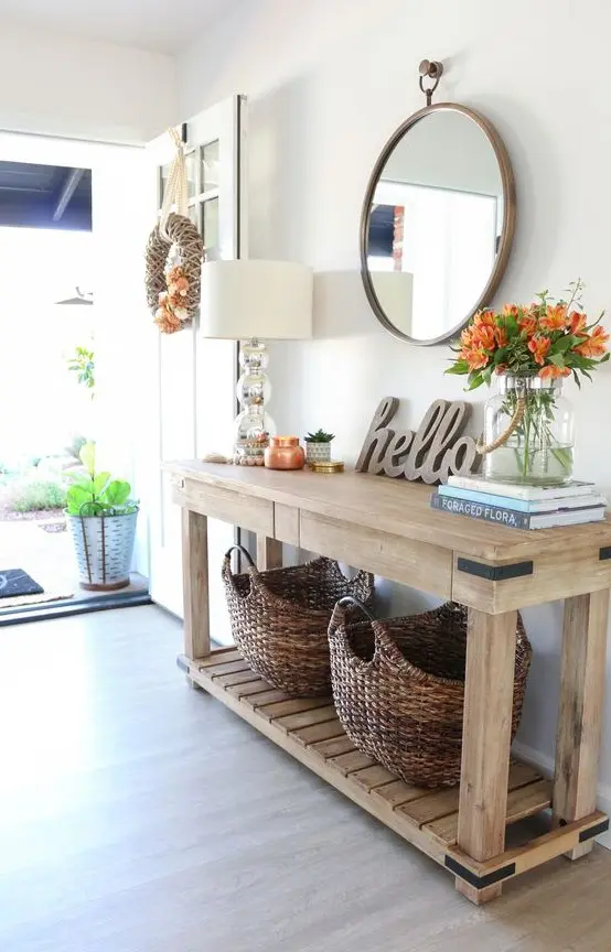 a farmhouse entryway with a wooden console table and baskets for storage, bright blooms and a round mirror