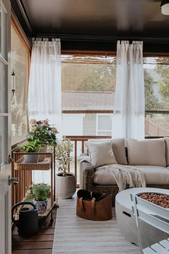 a farmhouse screened porch with wicker furniture, potted plants and blooms, a mobile fire pit and some chairs is cool