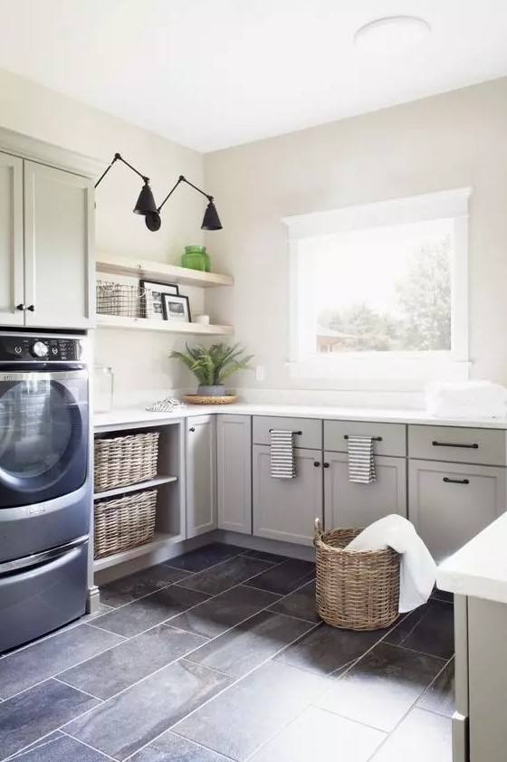 a grey farmhouse laundry with shaker style cabinets, a tiled floor, open shelving, navy appliances and baskets for storage