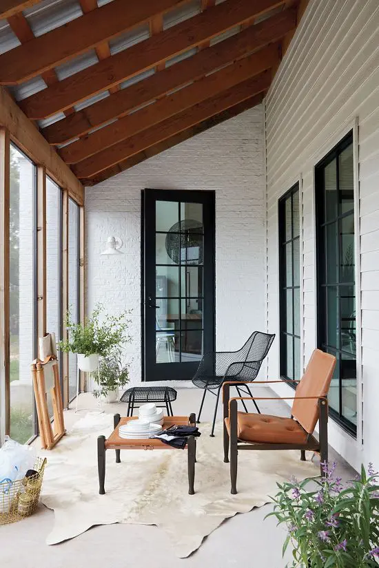 a modern farmhouse screened with a black metal chair and a footrest, an amber leather chair and an ottoman, greenery and a rug
