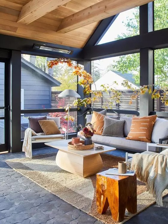 a modern screened porch with a grey modern sofa, white chairs, a coffee table and stained stool and some bright foliage