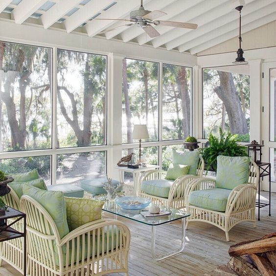 a neutral screened porch with white wicker chairs, a glass coffee table and aqua stools and potted greenery and lanterns