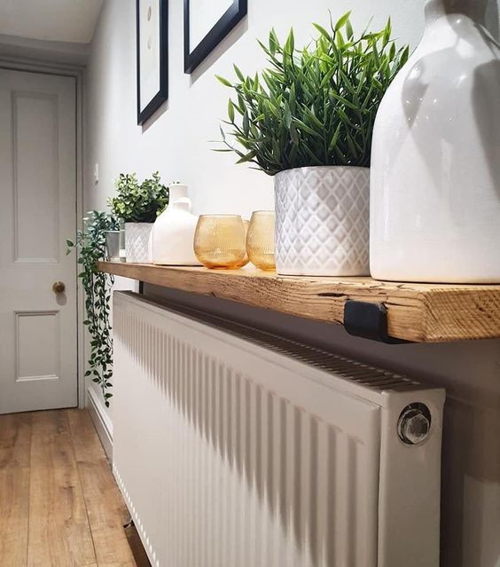 a radiator hidden with a light stained shelf that is used for storage and to display the plants