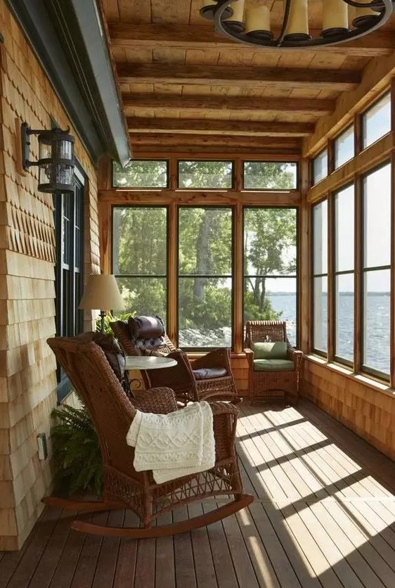 a rustic screened porch with wicker rockers, a coffee table and a table lamp, potted greenery and a cool lake view