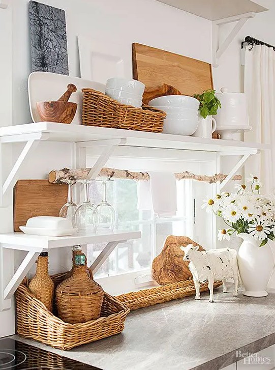 a rustic white kitchen with open shelves, white porcelain and wicker baskets for storage, a branch for hanging towels is cozy