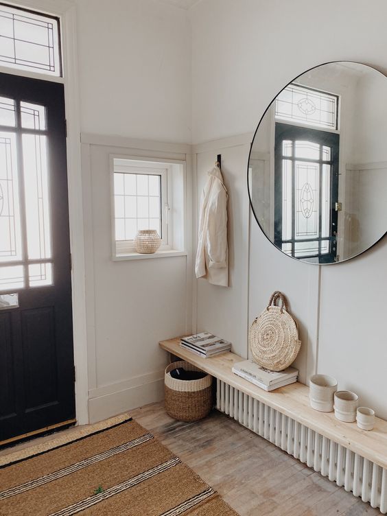 a small and welcoming entryway with paneling, a radiator with a shelf that is used for storage, a round mirror and some baskets