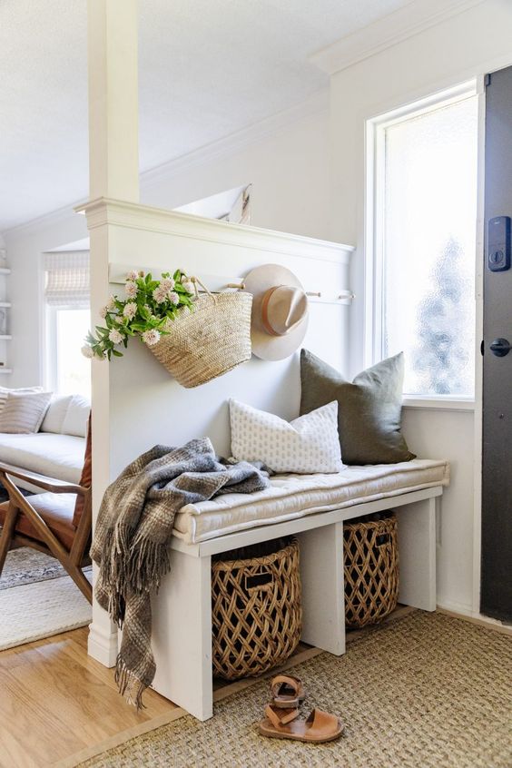 a small entryway bench with a cushion and pillows, baskets for storage and a straw bag with blooms
