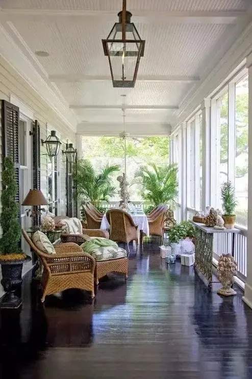 A vintage inspired screened porch with wicker furniture and printed upholstery, potted plants and decor and lanterns