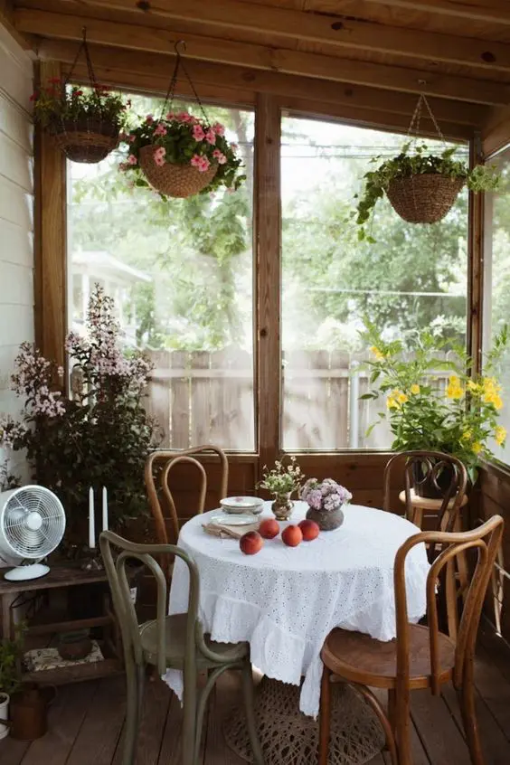 a vintage screened porch with a round table and wooden chairs, potted blooms and candles is a cozy nook for having meals