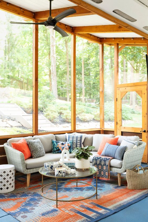 a vivacious screened porch with a wicker sofa with bright pillows, a tiered glass coffee table, a bright rug and a side table