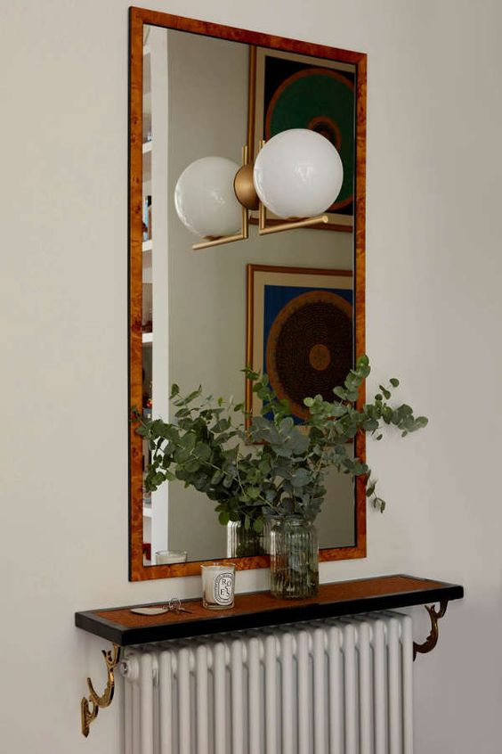a white radiator, a stained shelf that turns it into a console table, a mirror, a lamp and some greenery for a small entryway