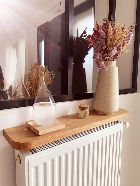 a white radiator with a light-stained shelf over it, some dried blooms and candles to make the radiator look cohesive
