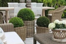 an outdoor space with timeless elegance. with wicker chairs, a sofa and stools, with a wicker table, white upholstery and lots of potted greenery