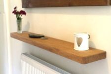 a soild oak floating shelf installed over a radiator is a cool idea for a hallway, where there’s always not enough storage space