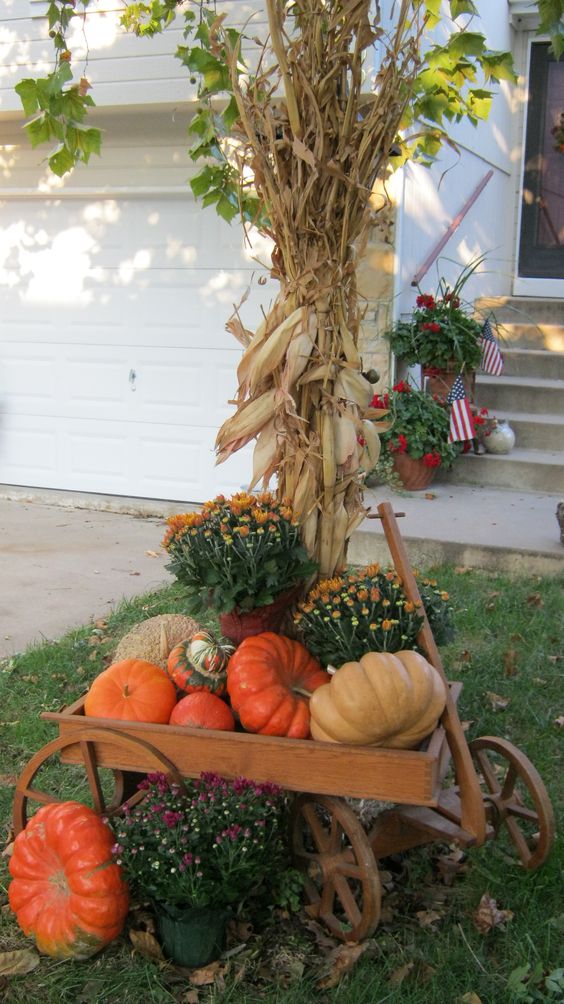 faux pumpkins and potted flowers displayed on a wooden trolley and corn husks