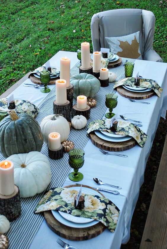 outdoor setting with white and gilded pumpkins and candles on wood stands