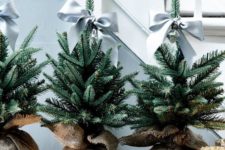 a trio of Christmas trees wrapped in burlap, with grey bow toppers is a cool solution for a farmhouse or rustic space