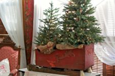 a duo of small Christmas trees in a small sleigh decorated with lights and ornaments is a cool idea for a rustic space