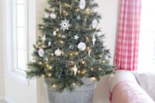 a small Christmas tree decorated with white ornaments and lights placed into a galvanized bucket is a cool rustic decor idea
