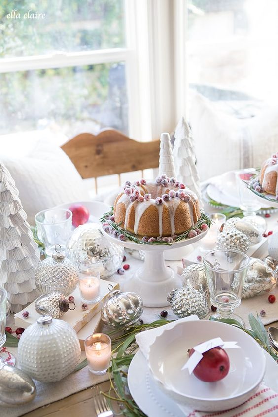 a beautiful Christmas table setting with a faux tree, large ornaments, white porcelain and red textiles, a bundt cake