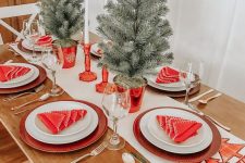 a colorful Christmas tablescape with a printed runner, red chargers, white porcelain, red napkins, mini trees and red candleholders with candles