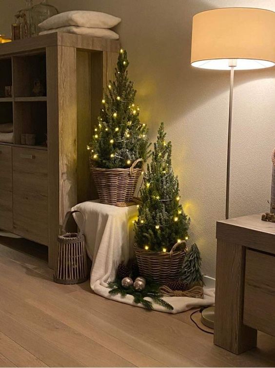 a duo of small Christmas trees in baskets, decorated with lights, are perfect for a rustic or Provence space