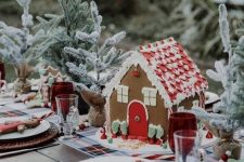 a lovely christmas tea party table with a plaid runner, a gingerbread house, evergreens, woven placemats, gingerbread cookies and printed napkins