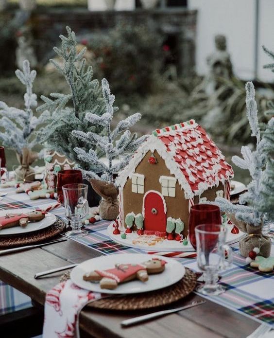 a lovely christmas tea party table with a plaid runner, a gingerbread house, evergreens, woven placemats, gingerbread cookies and printed napkins
