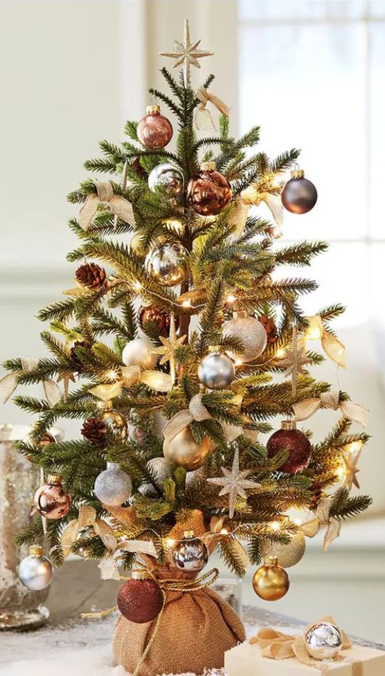 a mini Christmas tree decorated with silver, grey, gold and brown ornaments and lights