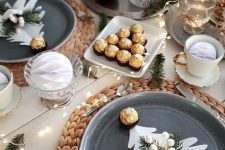 a modern Christmas tea party table with wovne placemats, grey plates, sweets and candies, lights and evergreens