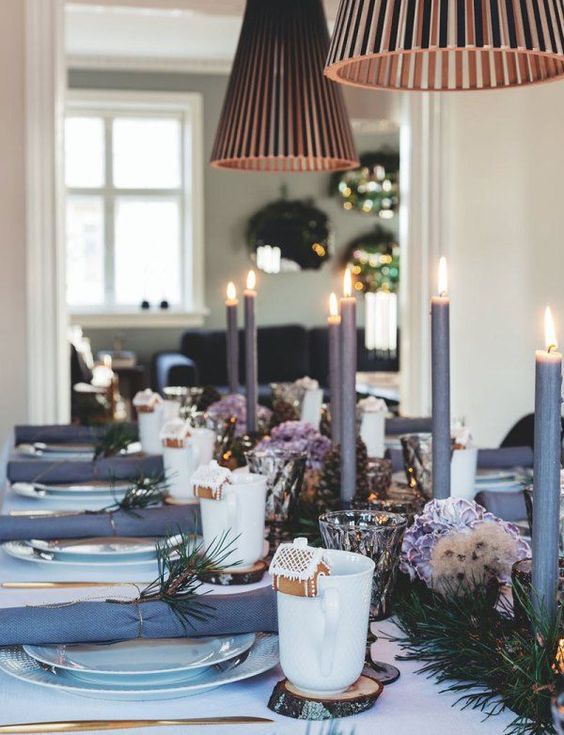 a refined Christmas table setting with mauve napkins and candles, white porcelain, gold cutlery and gingerbread houses and evergreens