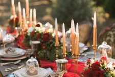 a refined Christmas tablescape with a red runner, red blooms, neutral candles, porcelain, printed napkins and gold glasses