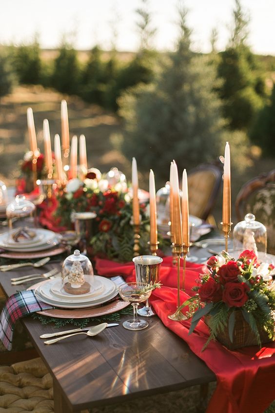 a refined Christmas tablescape with a red runner, red blooms, neutral candles, porcelain, printed napkins and gold glasses