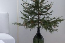 a small Christmas tree in a large green bottle with candles is a cool idea for a modern or Scandinavian space