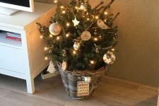 a small Christmas tree placed in a basket and styled with ornaments, lights and stars looks amazing