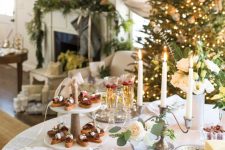 a stylish Christmas tea party table with all kinds of sweets and cookies served here, candles and blooms and greenery in a vase