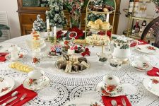 a vintage-inspired Christmas tablescape with a doily tablecloth, tiered stands with sweets and evergreens, printed plates and red napkins