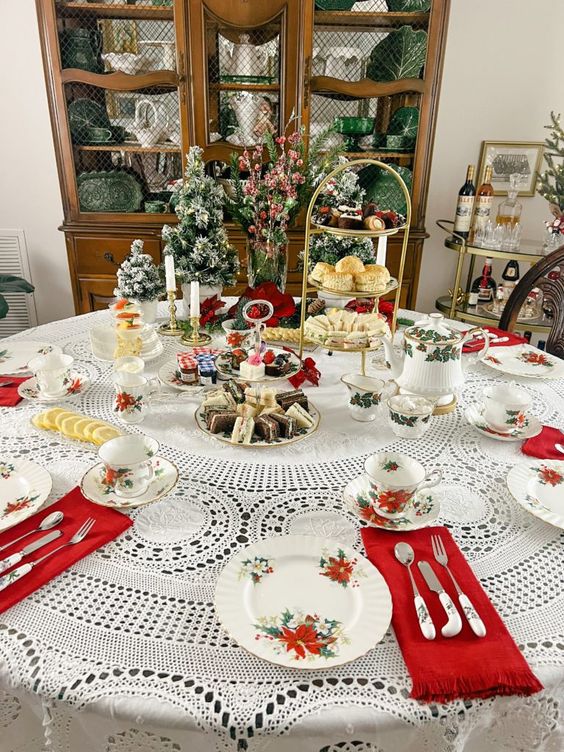 a vintage inspired Christmas tablescape with a doily tablecloth, tiered stands with sweets and evergreens, printed plates and red napkins